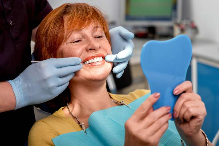 Woman checking her teeth in a dental clinic mirror after getting custom dentures in Bastrop, TX.